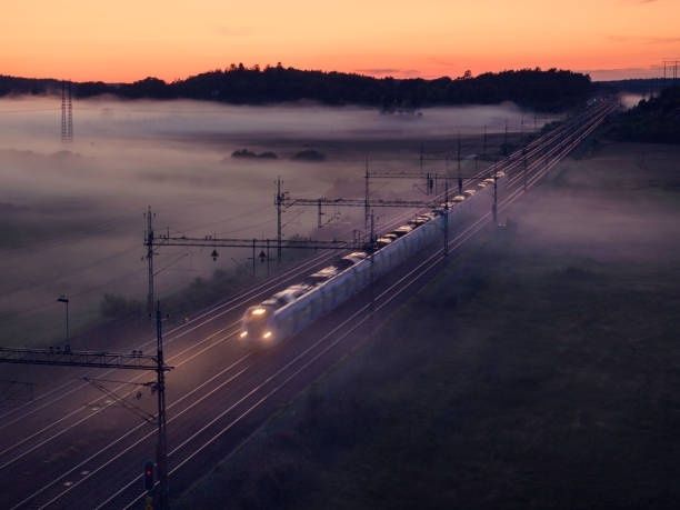 Pendeltåg färdas genom dimma över ett landskap i gryningsljus